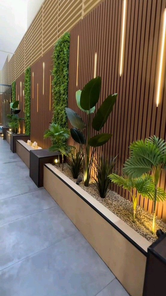 Corredor exterior revestido con panel listonado WPC color madera, luces LED verticales, jardines decorativos y plantas tropicales.