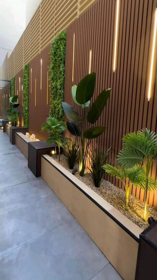 Corredor exterior revestido con panel listonado WPC color madera, luces LED verticales, jardines decorativos y plantas tropicales.