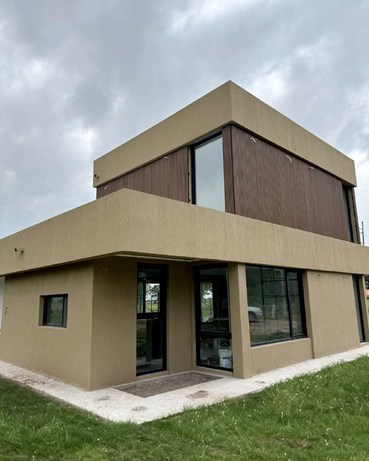 Casa moderna de dos pisos con revestimiento WPC color madera en la planta superior, ventanas negras y acabado beige.