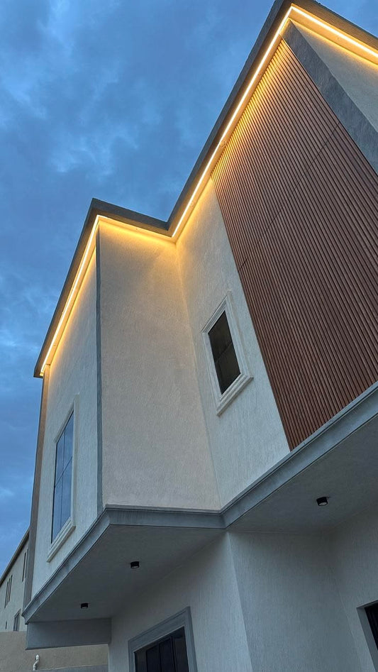Fachada moderna de dos pisos con revestimiento WPC color madera e iluminación LED cálida alrededor de la cubierta.
