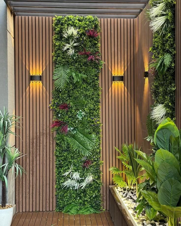 Jardín vertical decorativo combinado con revestimiento exterior WPC color madera, plantas tropicales e iluminación LED cálida.