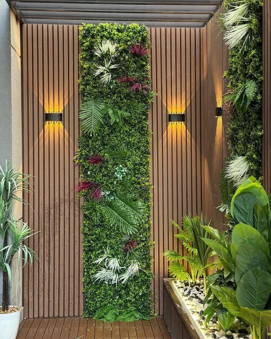 Jardín vertical decorativo combinado con revestimiento exterior WPC color madera, plantas tropicales e iluminación LED cálida.