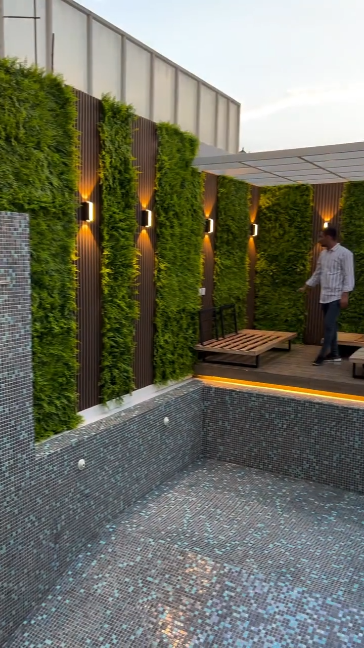 Zona de piscina decorada con paneles WPC color madera, jardines verticales e iluminación LED cálida en los muros.